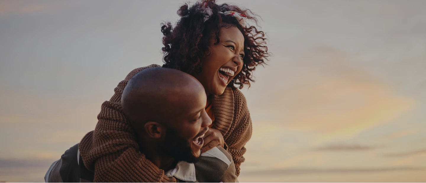 A joyful couple laughs together outdoors during a piggyback ride at sunset