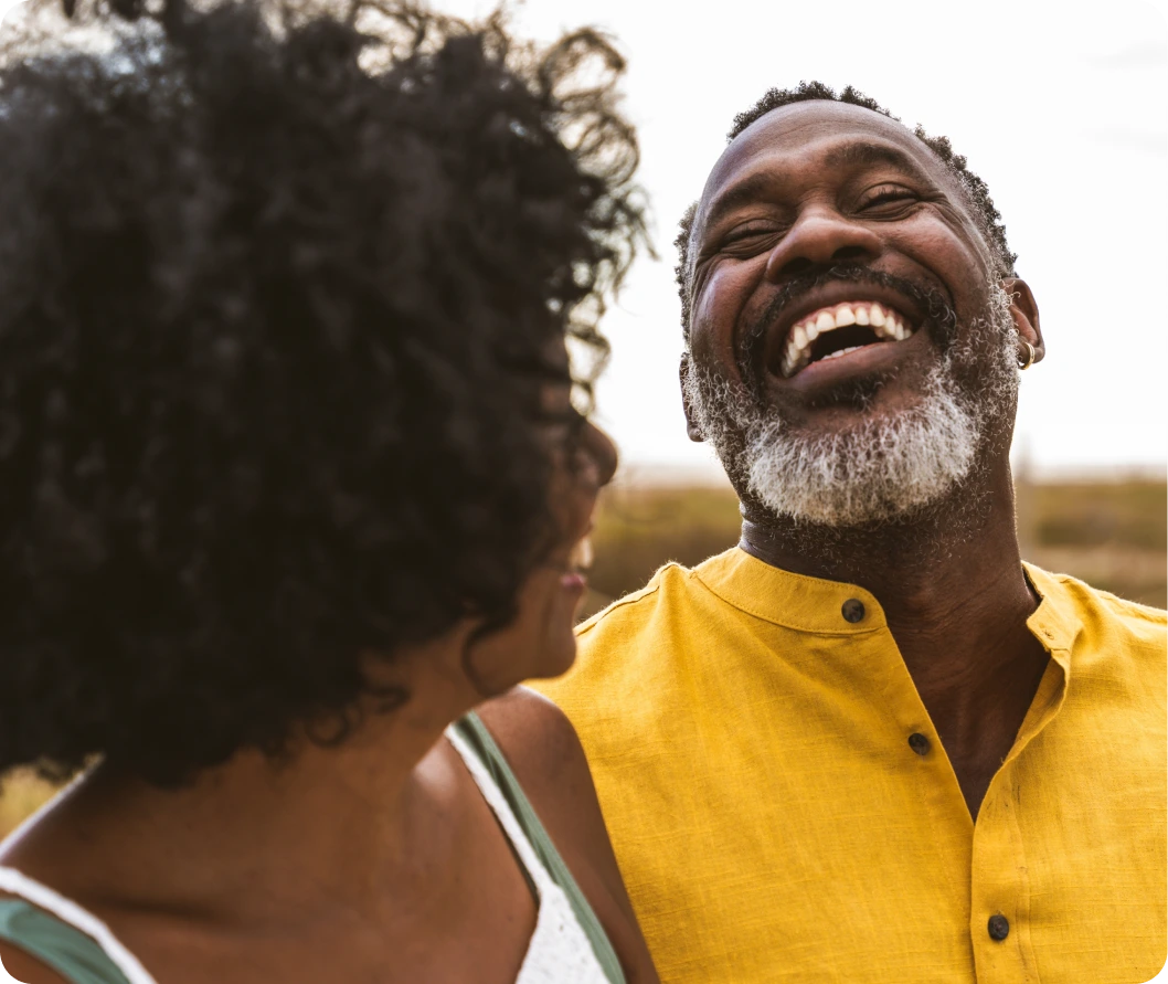 Man in yellow shirt laughing while talking with a woman outdoors
