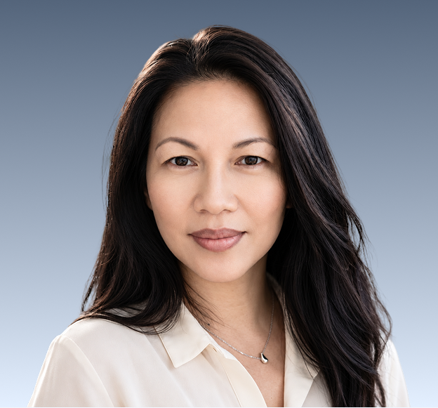 Professional headshot of a woman with long dark hair wearing a white collared shirt against a blue background