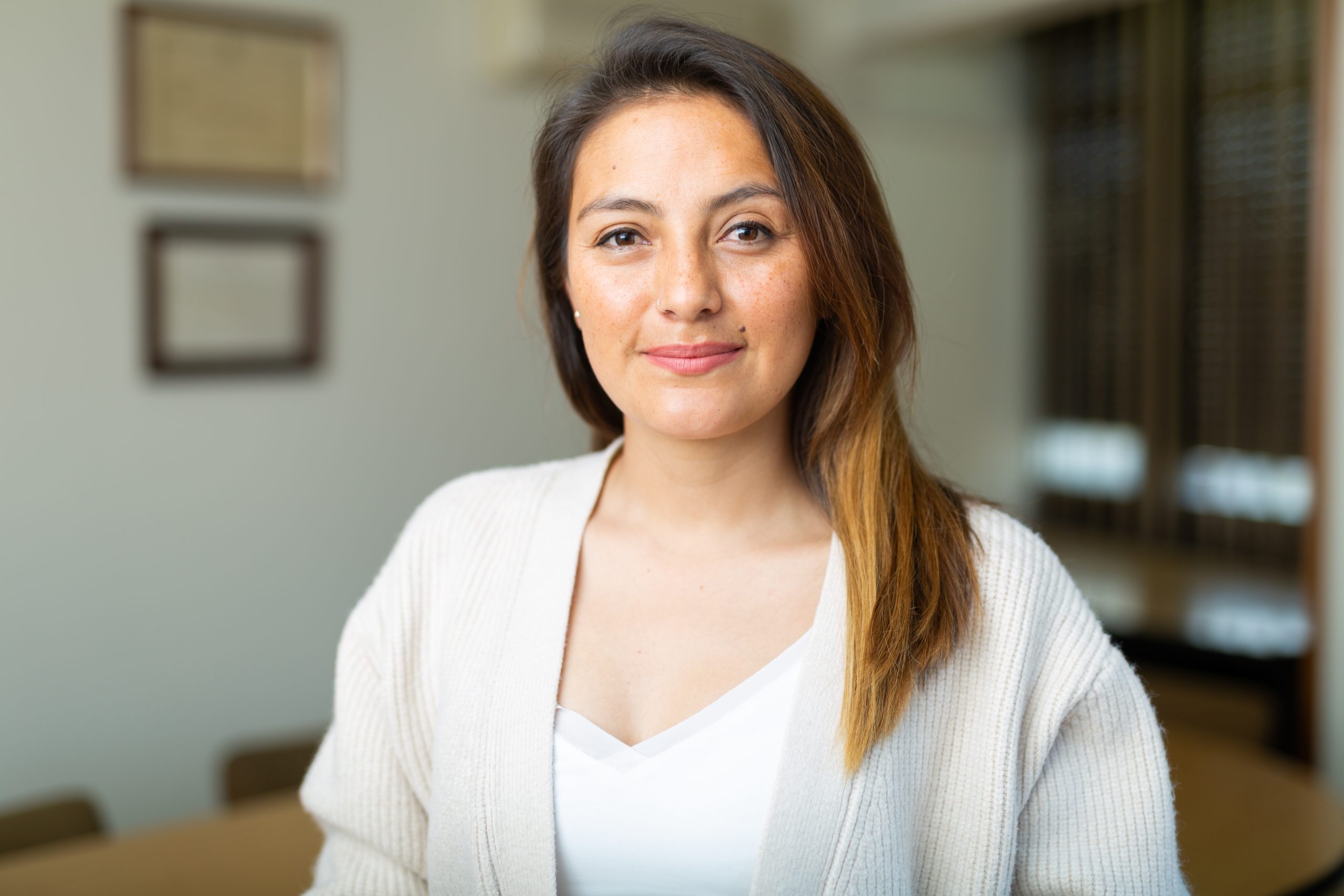 Woman smiling in an office setting, wearing a cream cardigan over white top