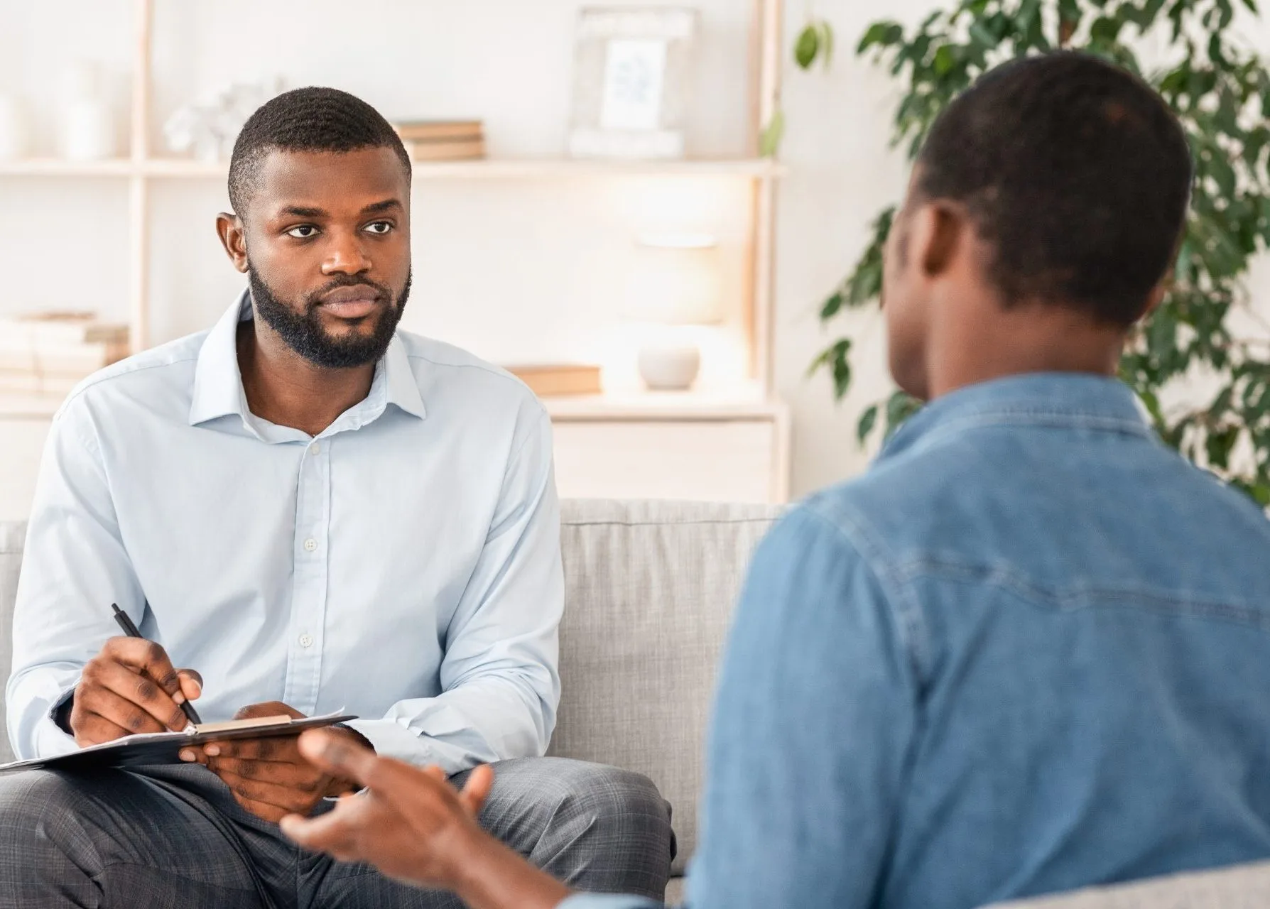 Therapist taking notes during a marital counseling session with a couple in a bright, modern office
