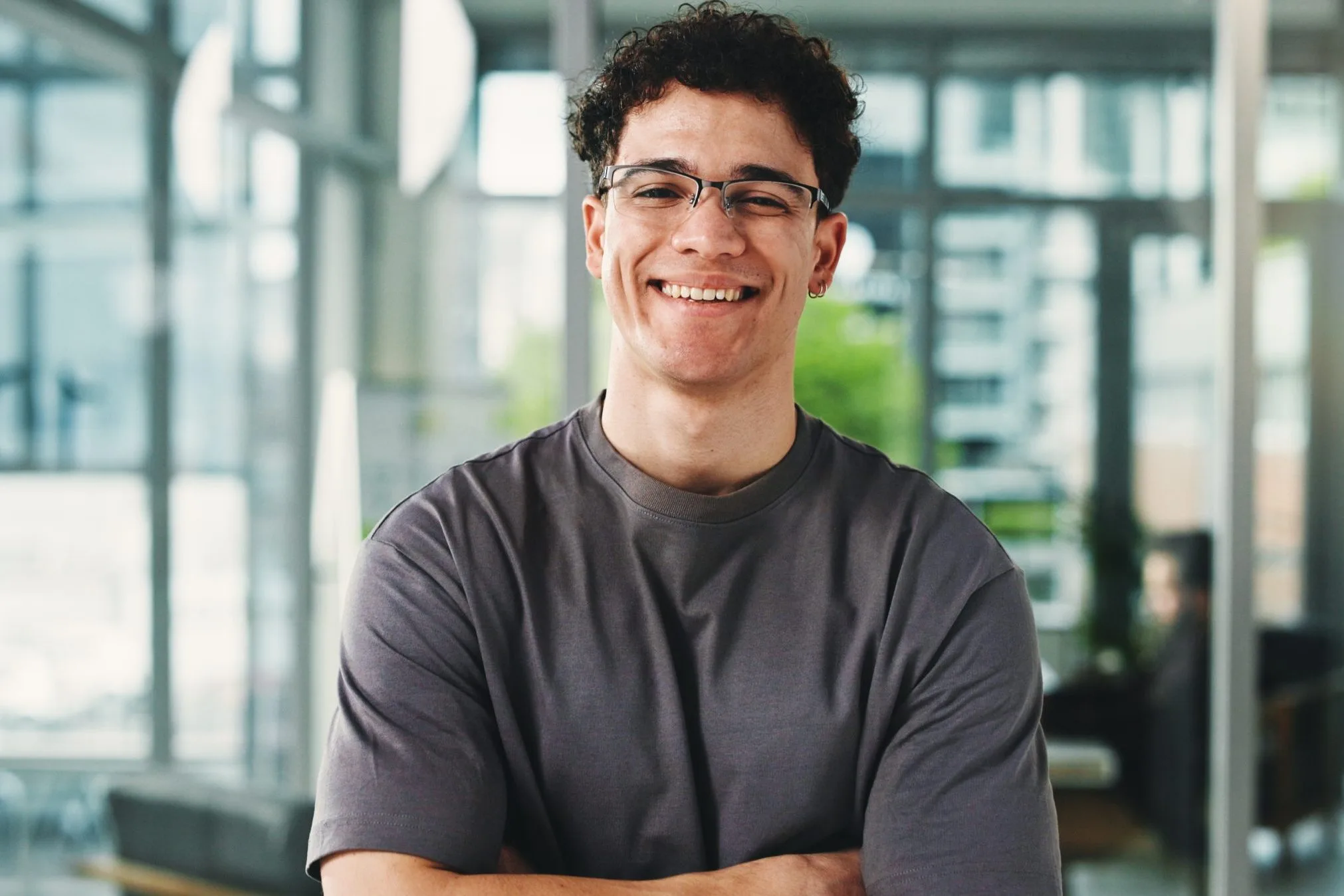 Man with glasses smiling in a modern office with large windows and city views