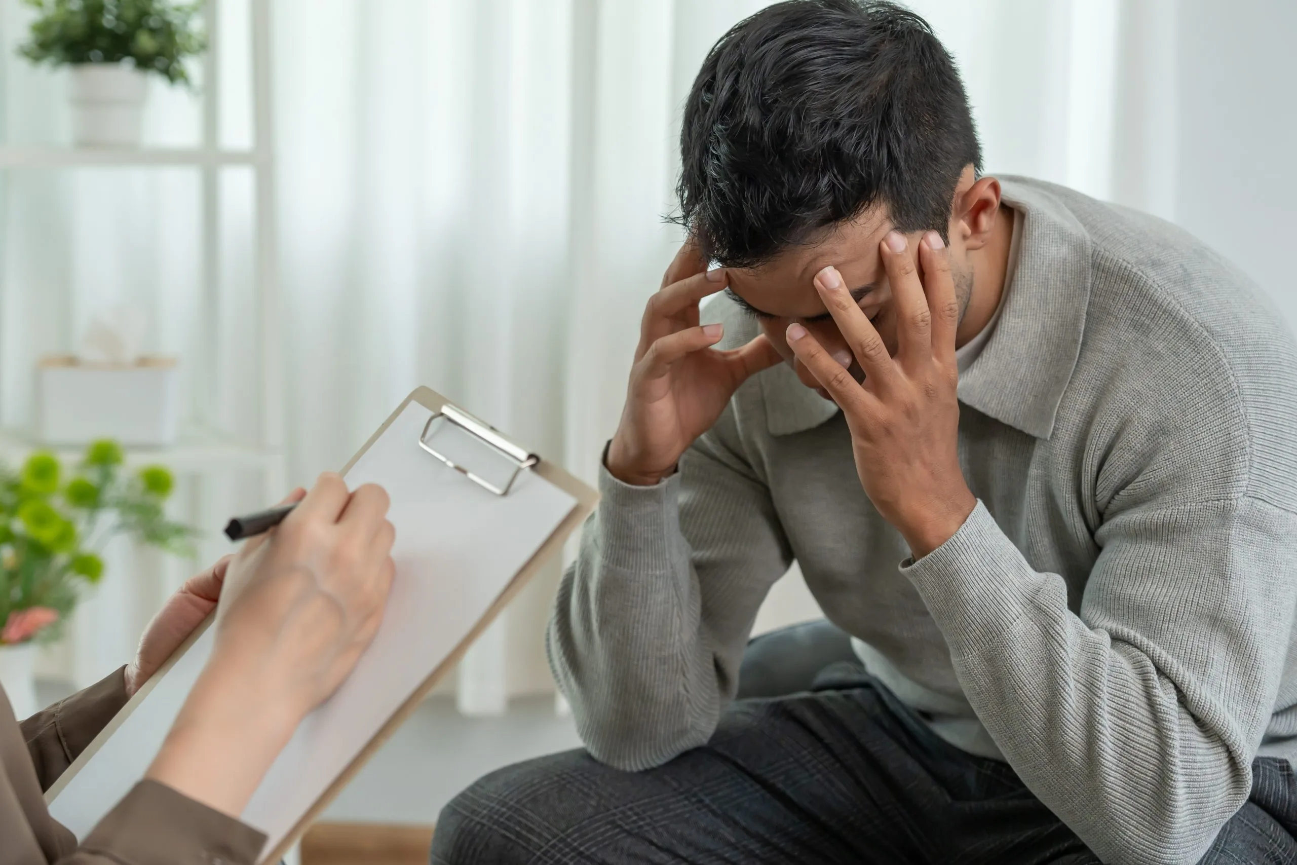 Man in distress during a mental health consultation with a therapist holding a clipboard