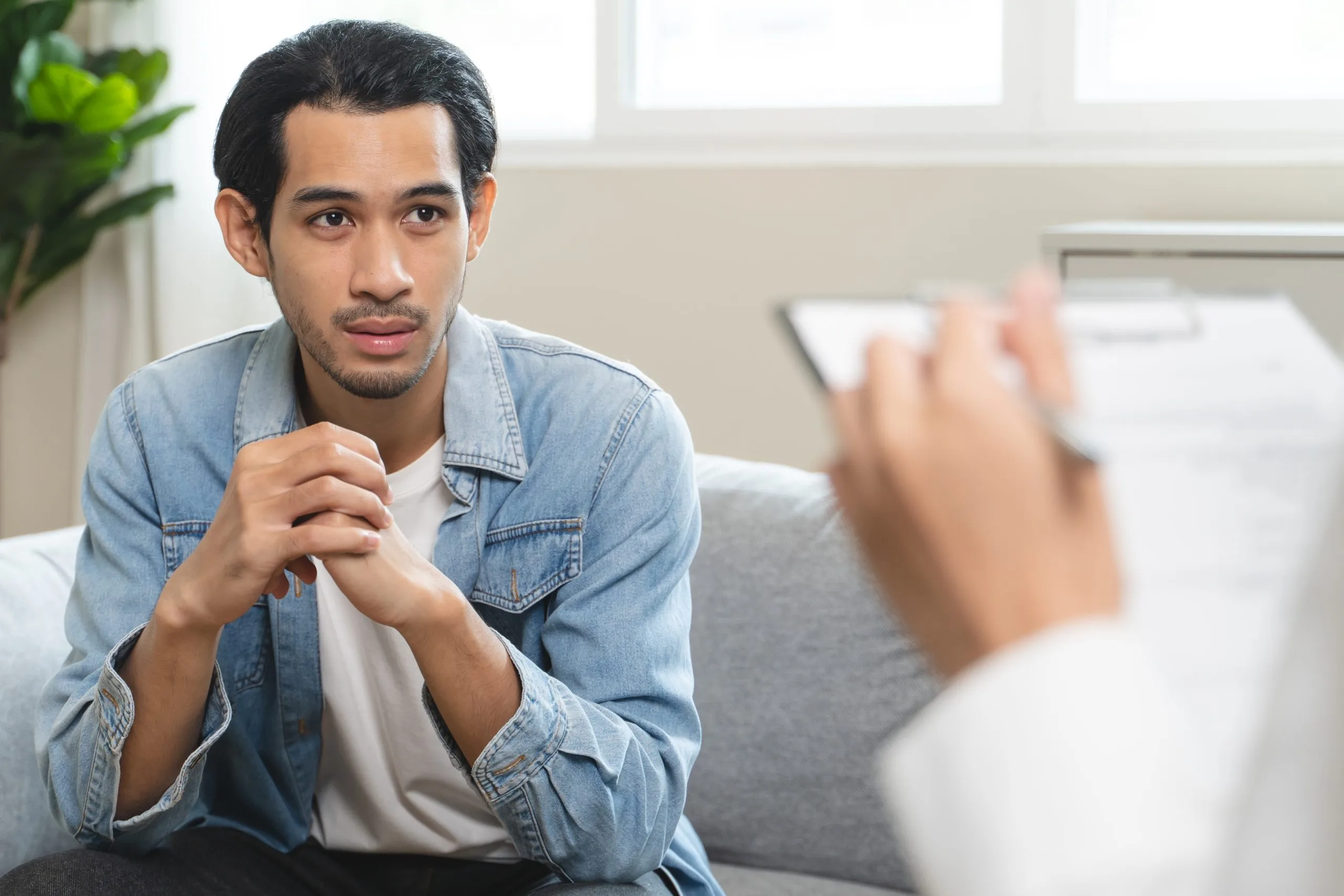 Man in denim shirt sitting on couch speaking with a therapist during a counseling session