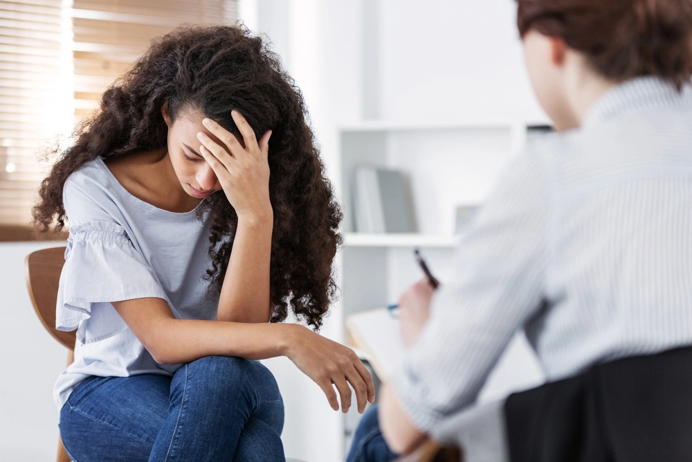 Distressed woman in therapy session, holding her head while therapist takes notes
