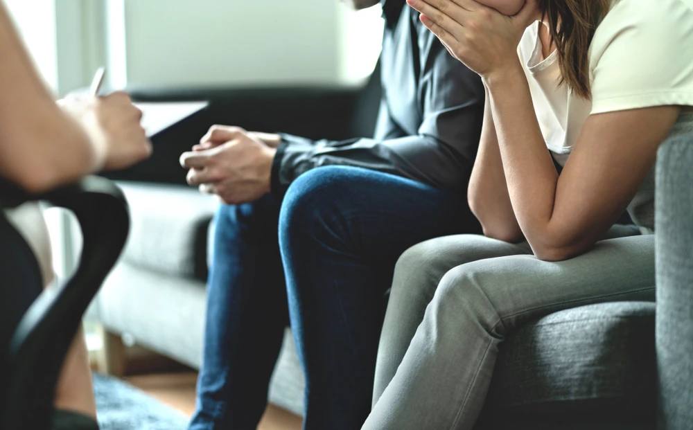 Couple attending counseling session, woman covering face in distress
