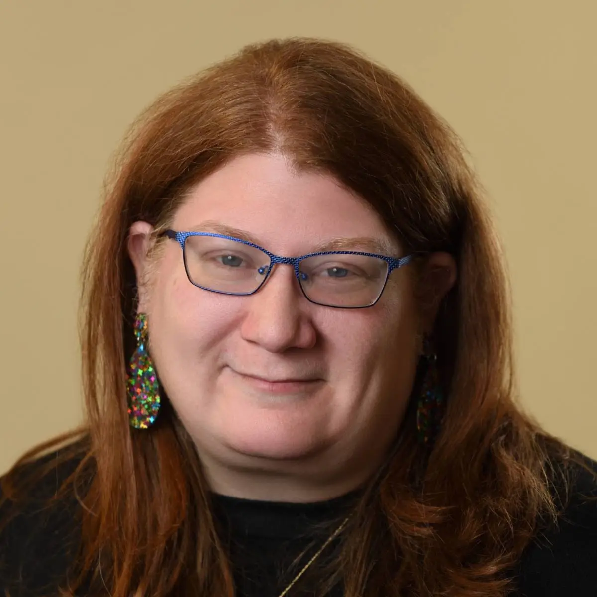 Diana Medd, LICSW, wearing blue glasses and colorful earrings, smiling at the camera