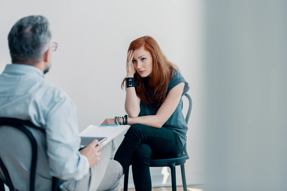 Young woman in therapy session with male counselor, discussing mental health and stress management in modern office