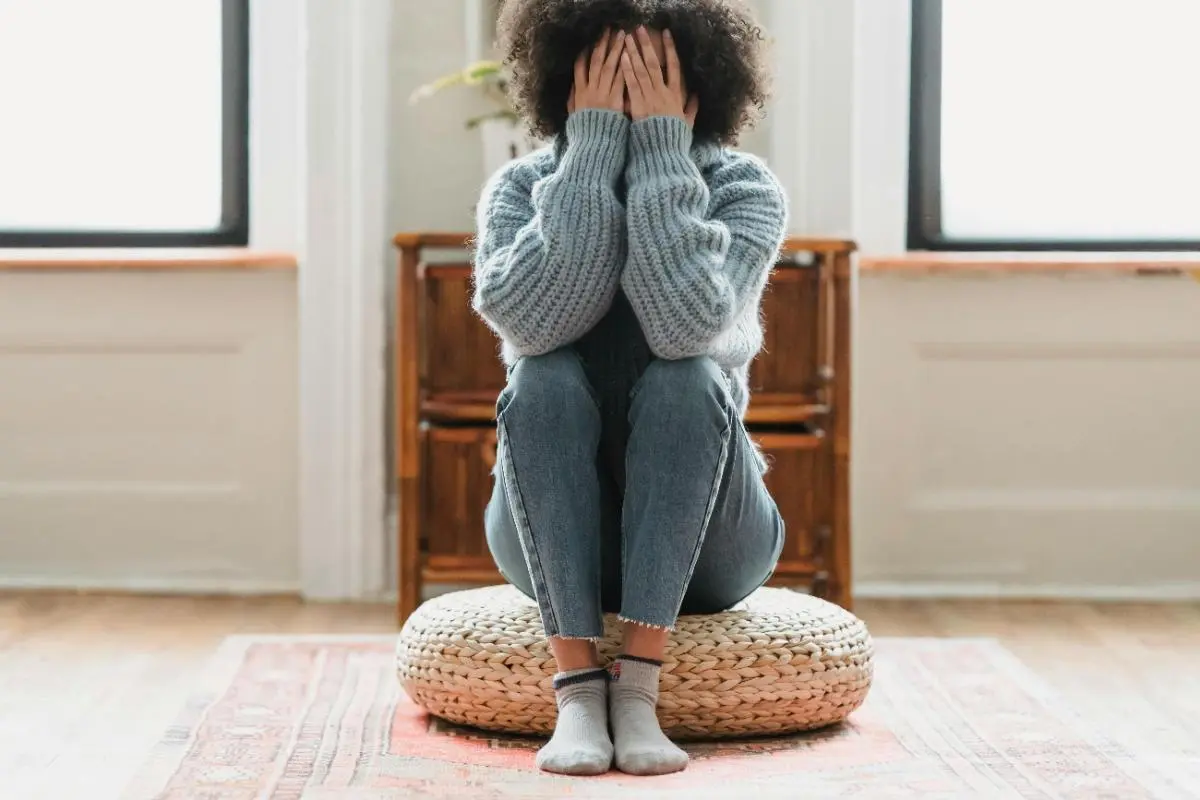 Person sitting on cushion with face in hands, showing stress or anxiety