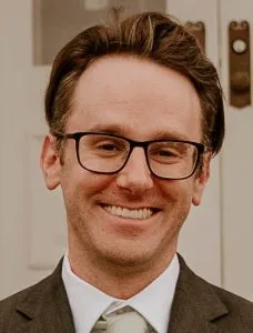 Aaron Baskin, LMHC, smiling at the camera wearing glasses and a brown blazer