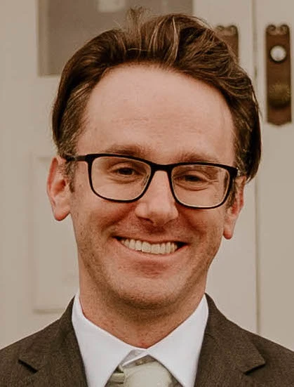 Aaron Baskin, LMHC, smiling at the camera wearing glasses and a brown blazer