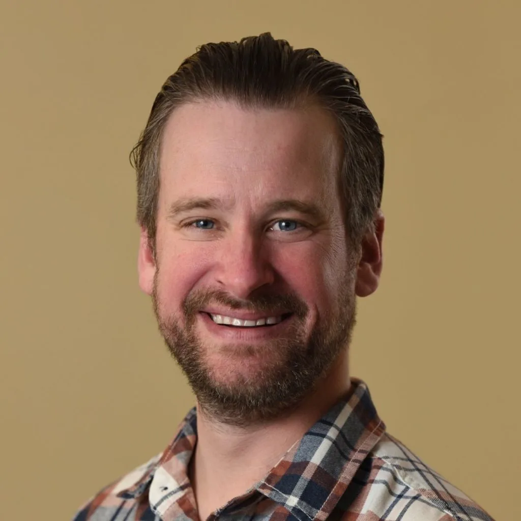 Larsen Bergen LMHC, therapist at The Psyched Group, smiling in a plaid shirt against a tan background