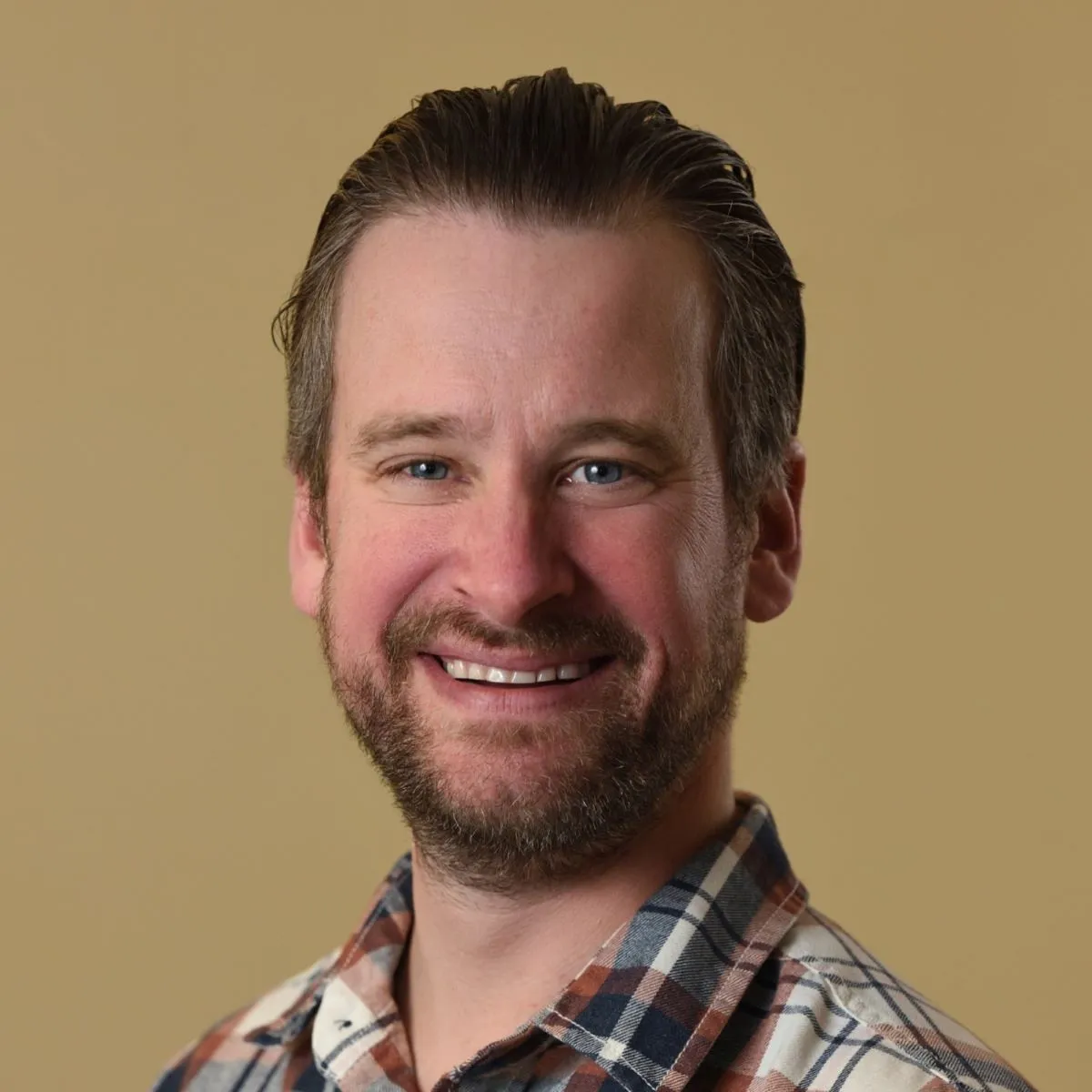 Larsen Bergen LMHC, therapist at The Psyched Group, smiling in a plaid shirt against a tan background