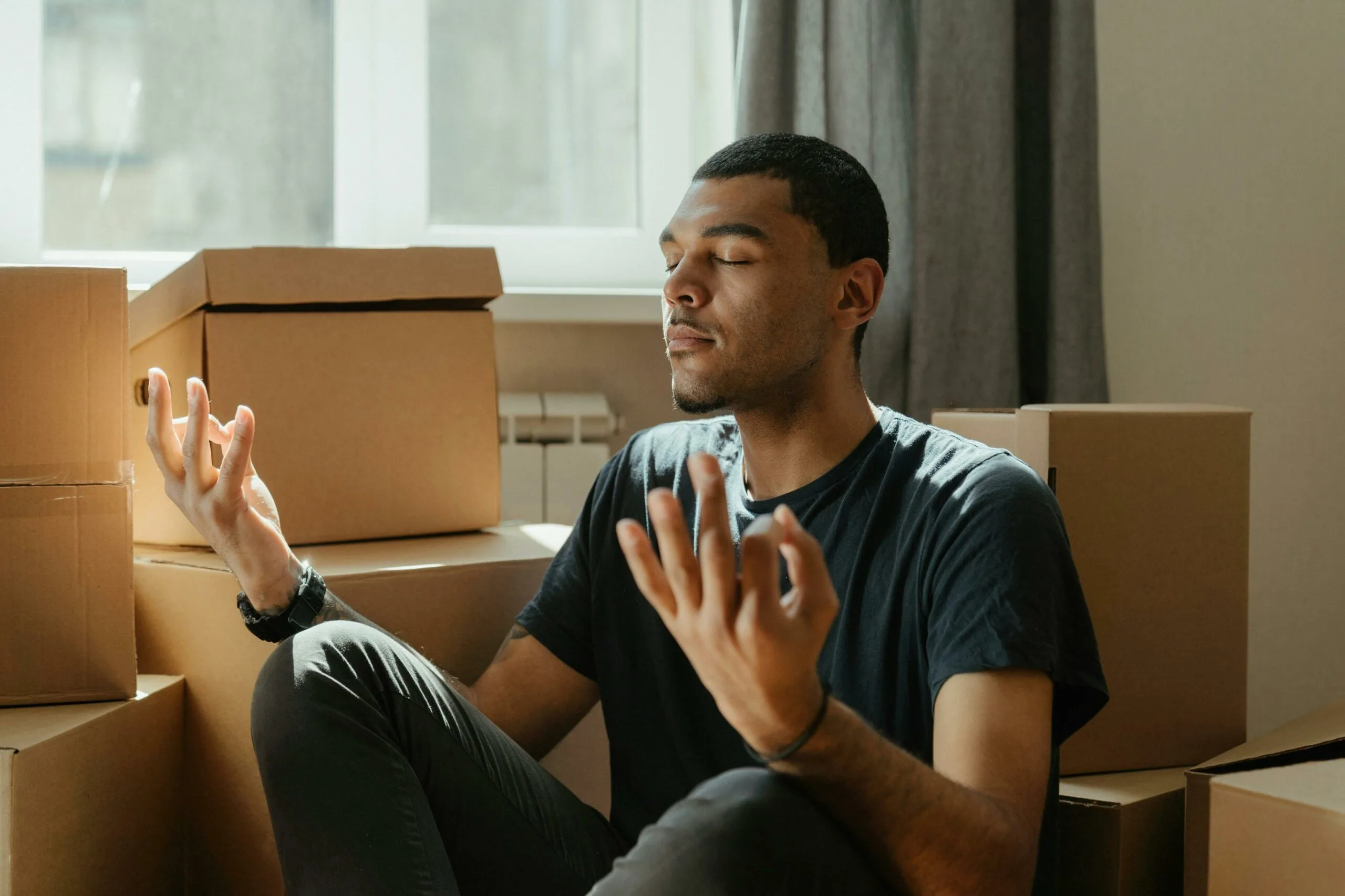 Man meditating in new home surrounded by moving boxes