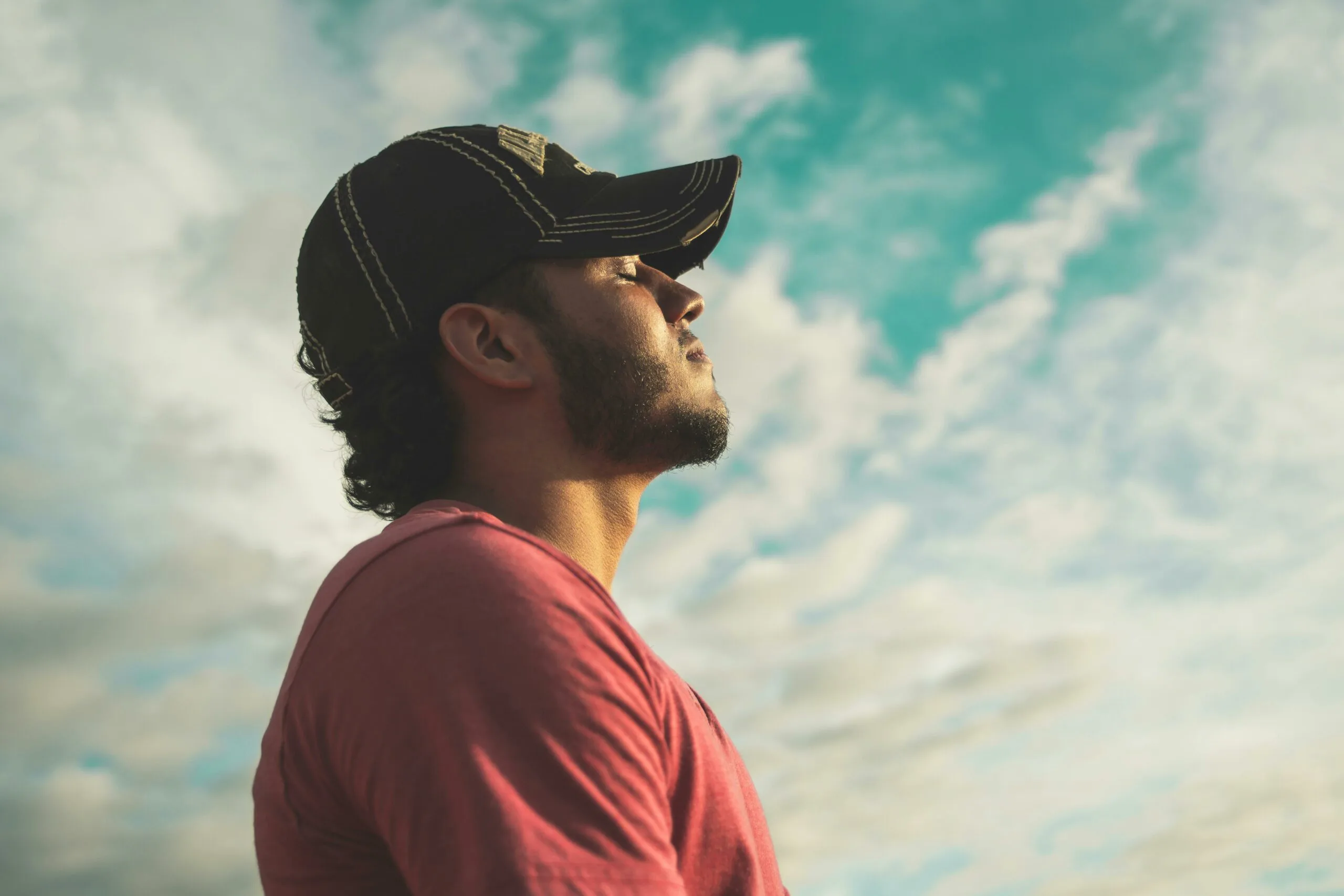 Man in red shirt looking up at the cloudy blue sky