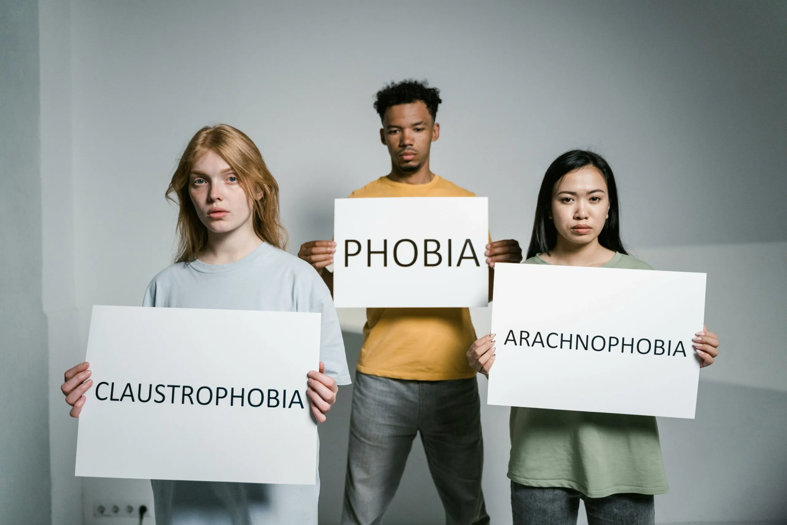 Three people holding signs reading claustrophobia, phobia and arachnophobia