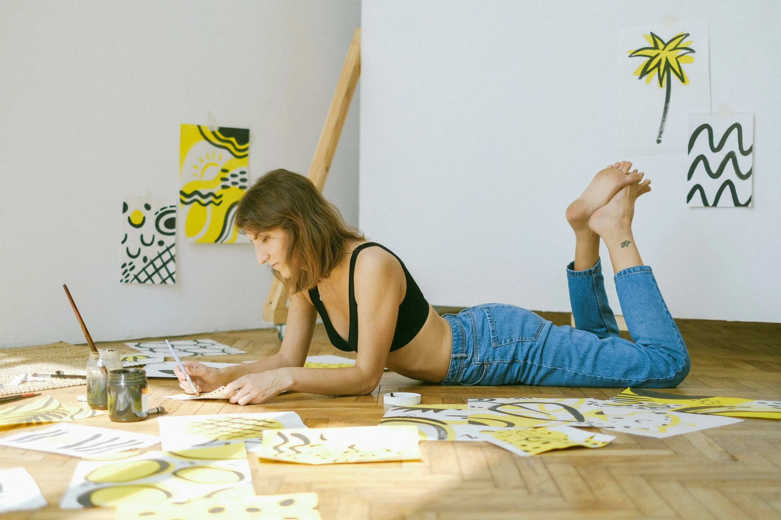 Young woman painting abstract art on floor surrounded by colorful sketches