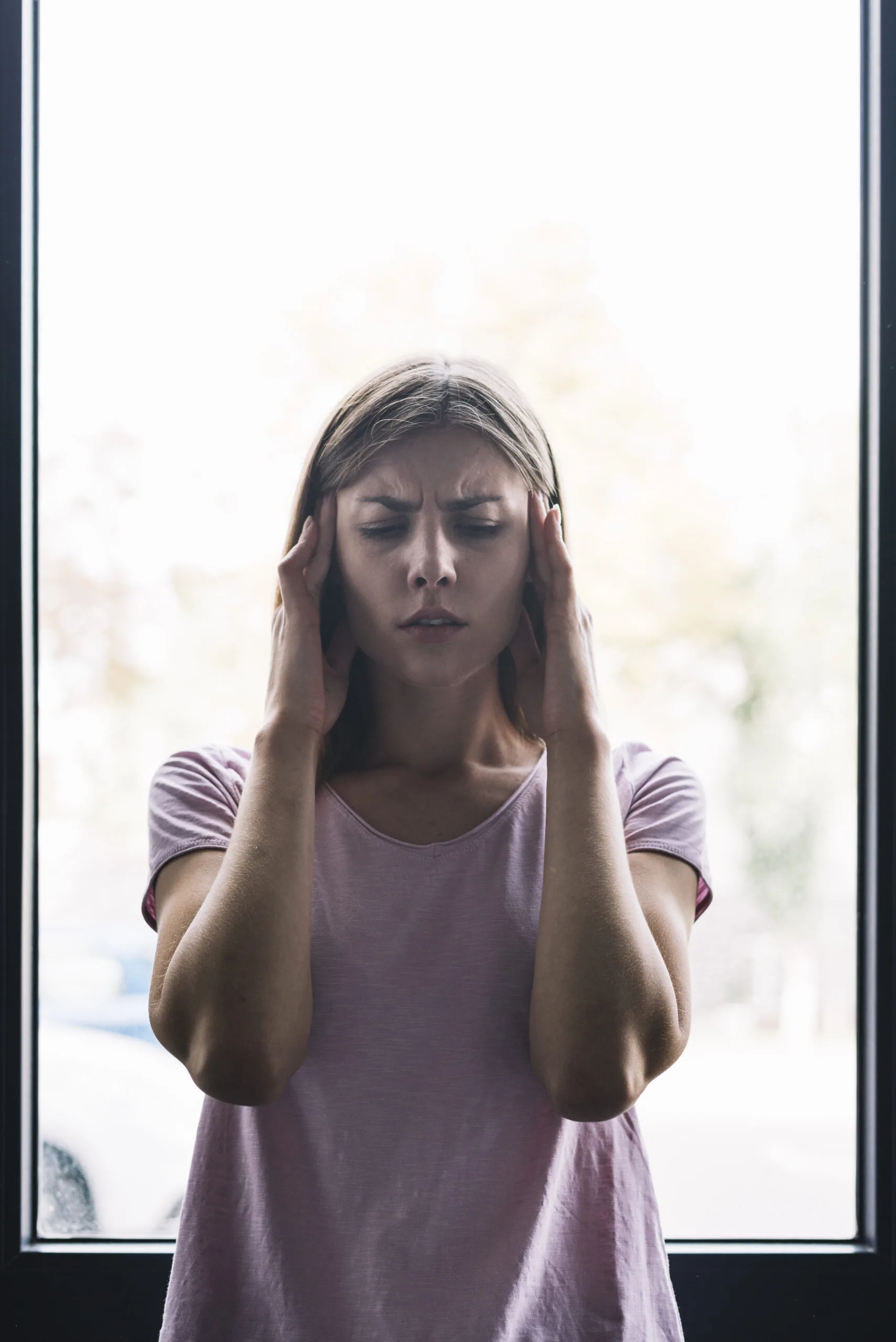 Young woman with headache holding her temples in front of wind