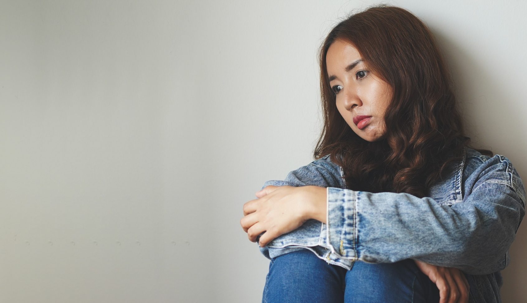 Young woman hugging her knees against a wall