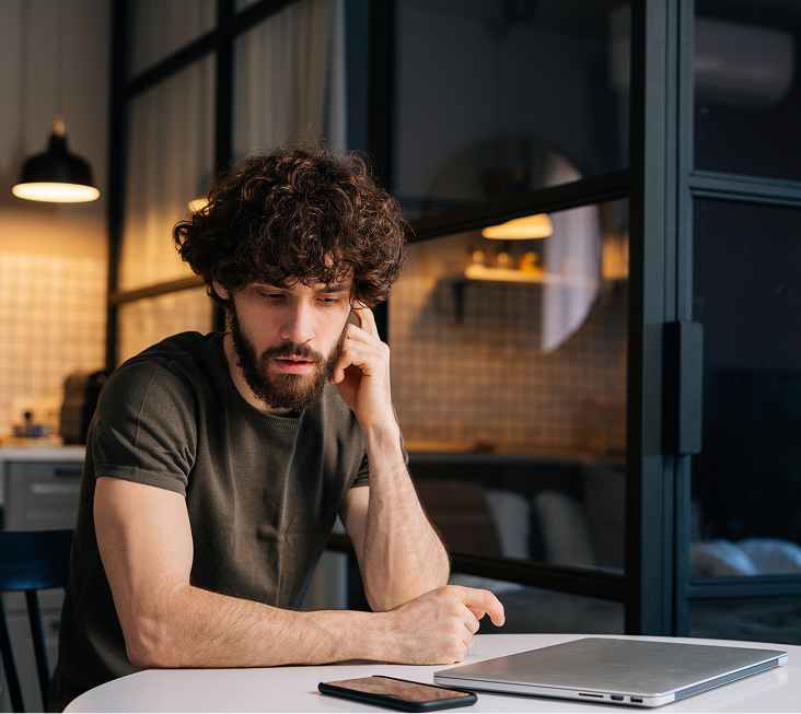 Man with anxious expression sitting at desk with laptop and phone