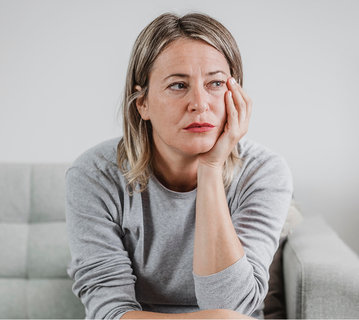 Woman sitting on couch with hand to face, appearing contemplative or distressed