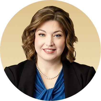 Professional headshot of a woman with shoulder-length brown wavy hair, pearl necklace, black blazer, and blue top against a tan circular background