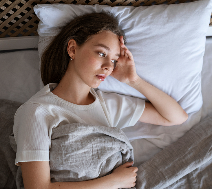 Woman lying in bed with hand to face, appearing uncomfortable or in discomfort