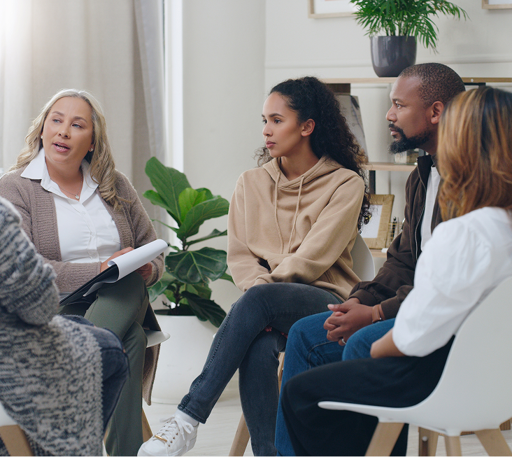 Therapist leading a family systems therapy session with four adults seated in a circle in a light-filled office