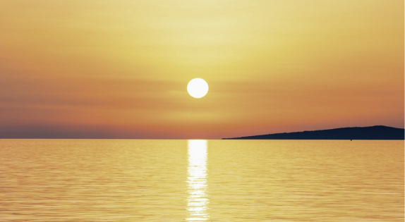 Sun setting over calm water with golden light reflecting on the surface
