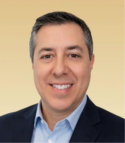 Middle-aged man with dark hair smiling at camera, wearing light blue shirt and dark blazer