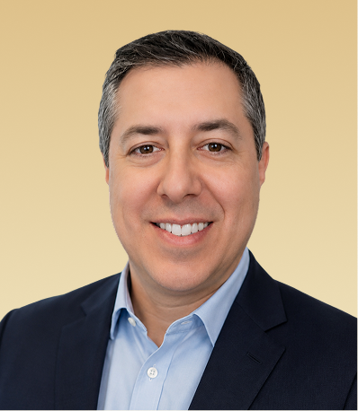 Professional headshot of a smiling man in a dark blazer and light blue shirt against a tan background