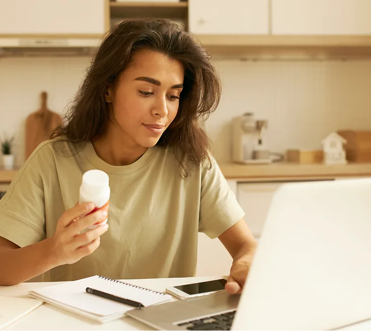 Woman in kitchen holding dental aligner while looking at laptop screen
