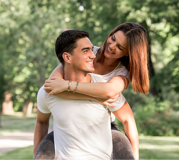 Couple smiling outdoors, man giving woman piggyback ride in park setting