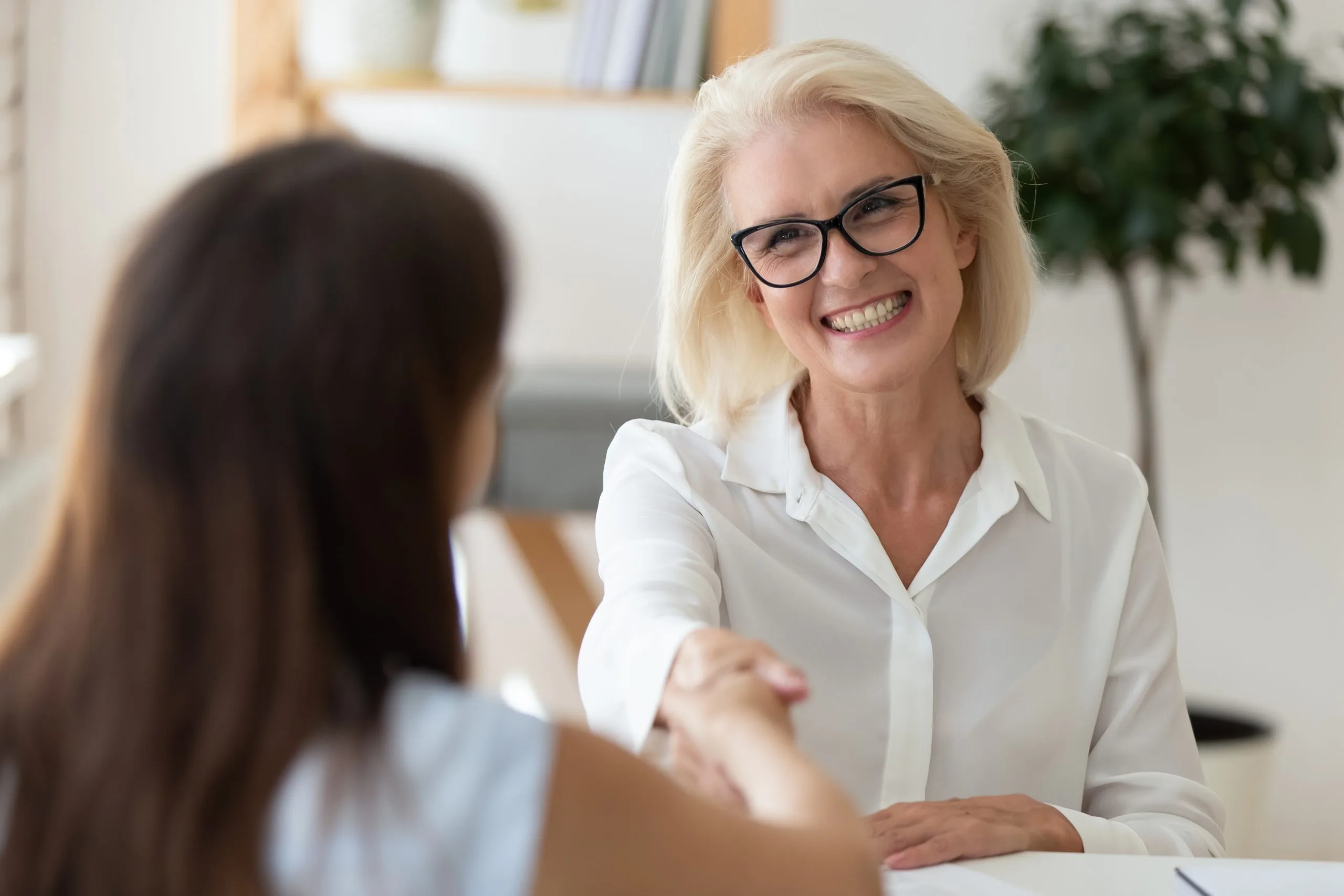 Female therapist in glasses shaking hands with a patient during a consultation