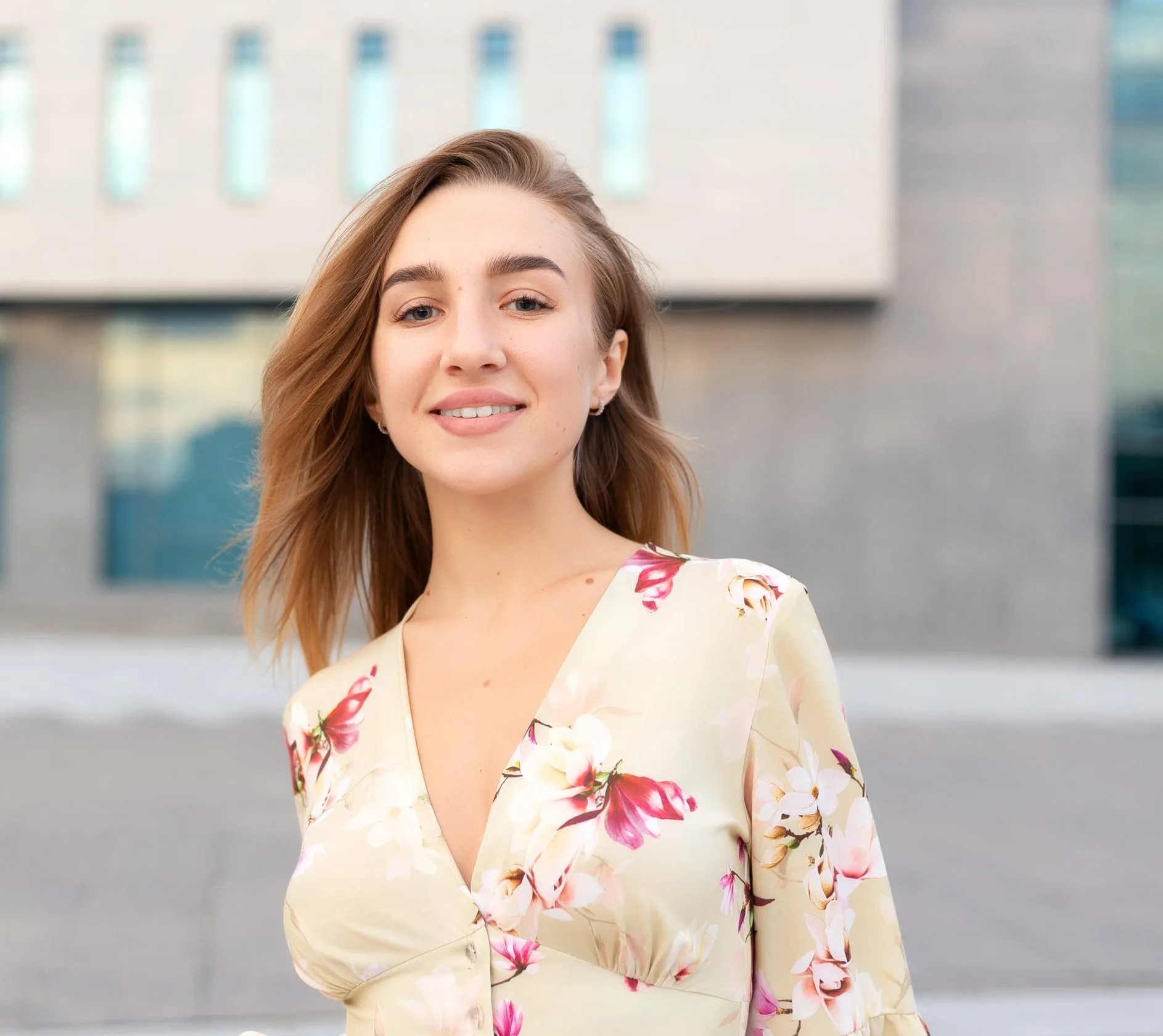 Woman smiling at camera in floral blouse against modern building exterior