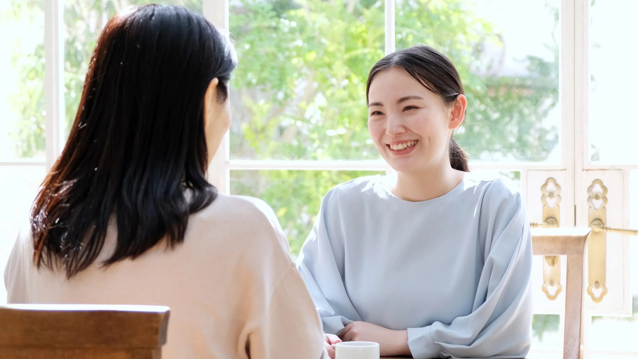 Two women having a friendly conversation by a bright window in a clinical setting