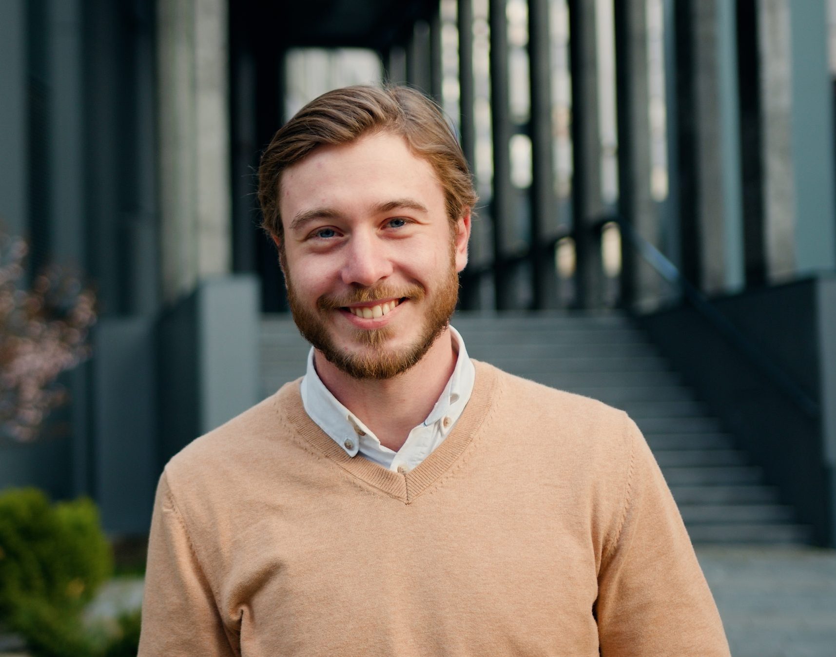 Man smiling at camera in beige sweater on modern building exterior