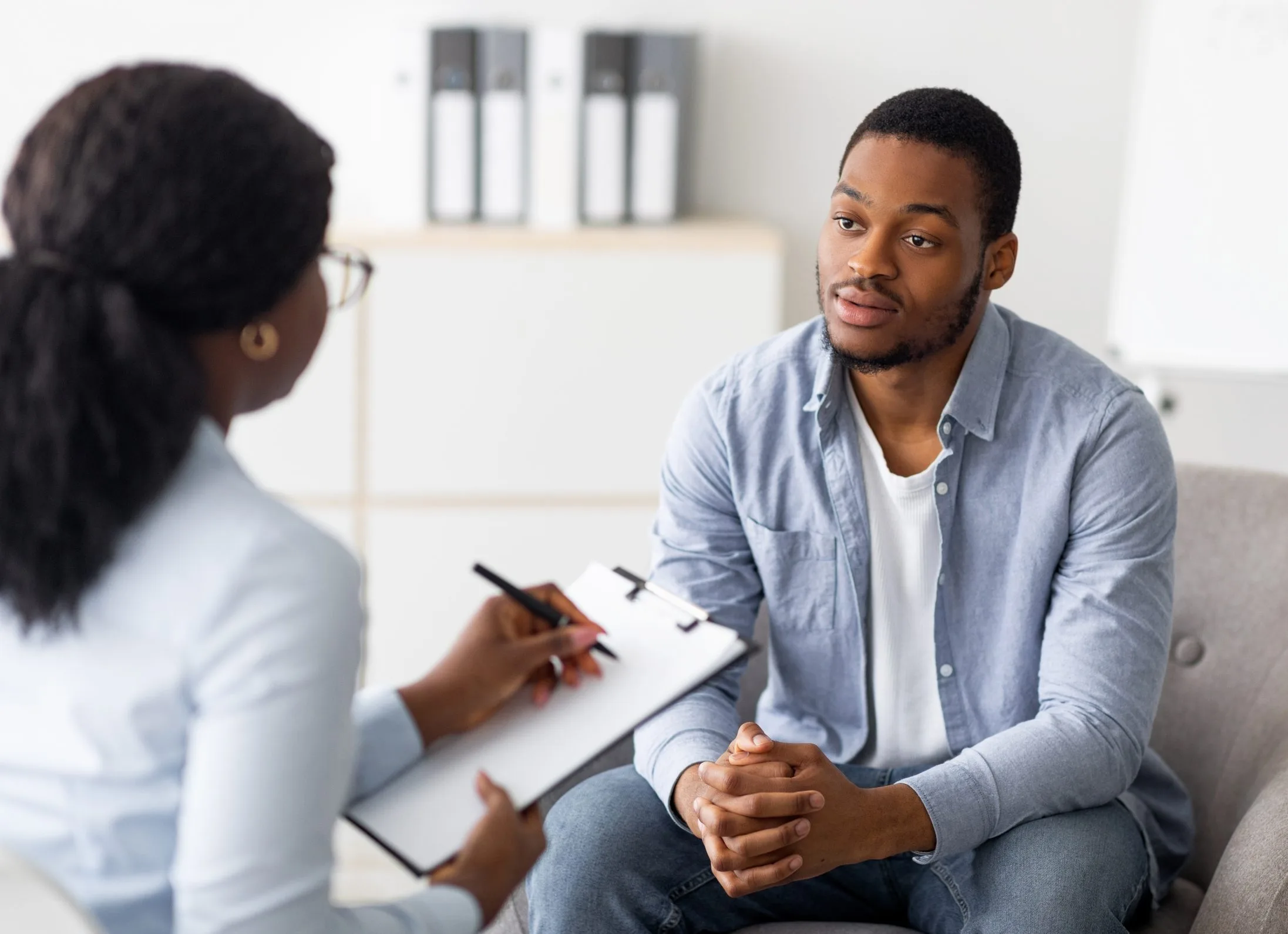 Therapist taking notes while listening to a male patient during a counseling session