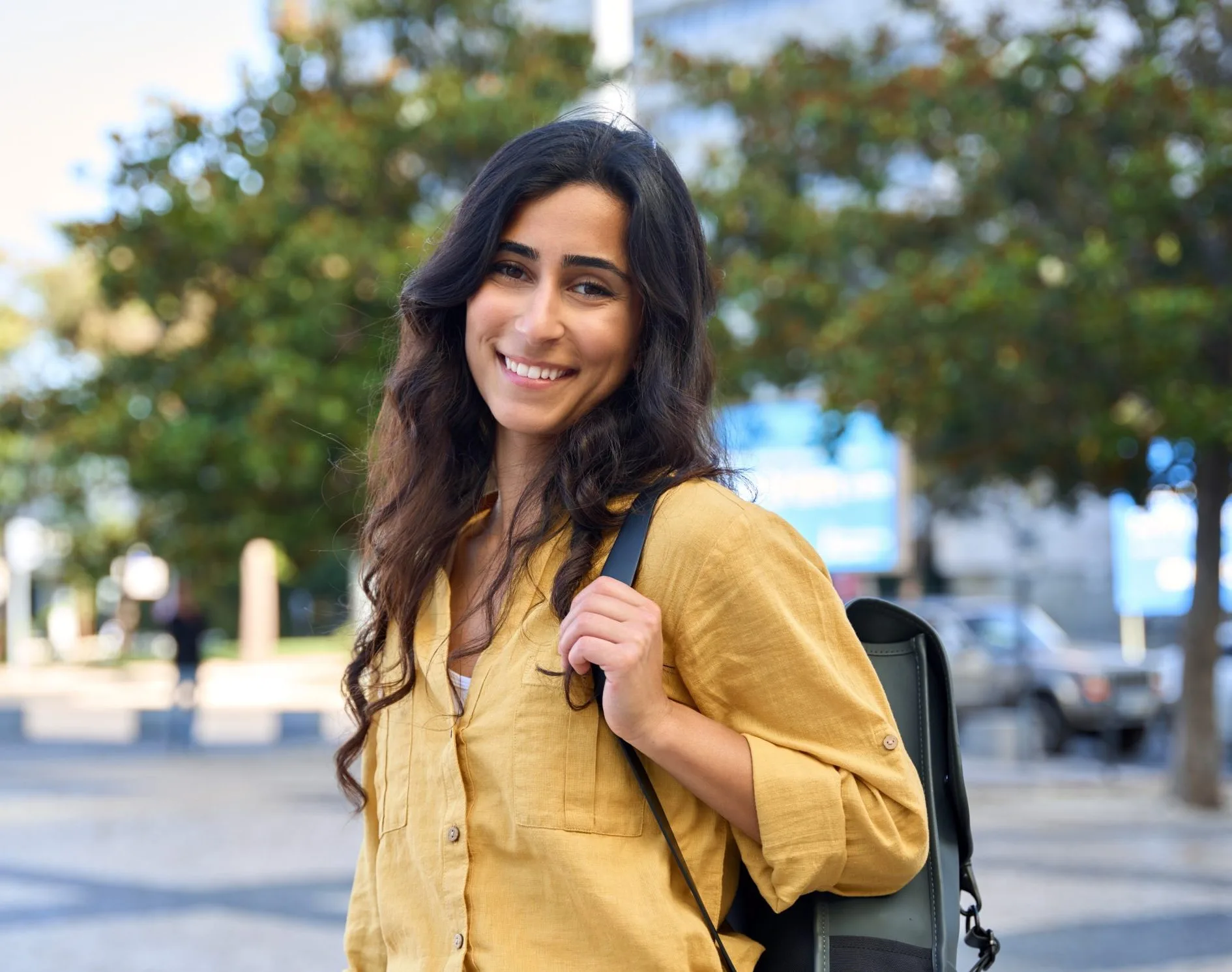 Woman in yellow shirt smiling at camera outdoors with backpack