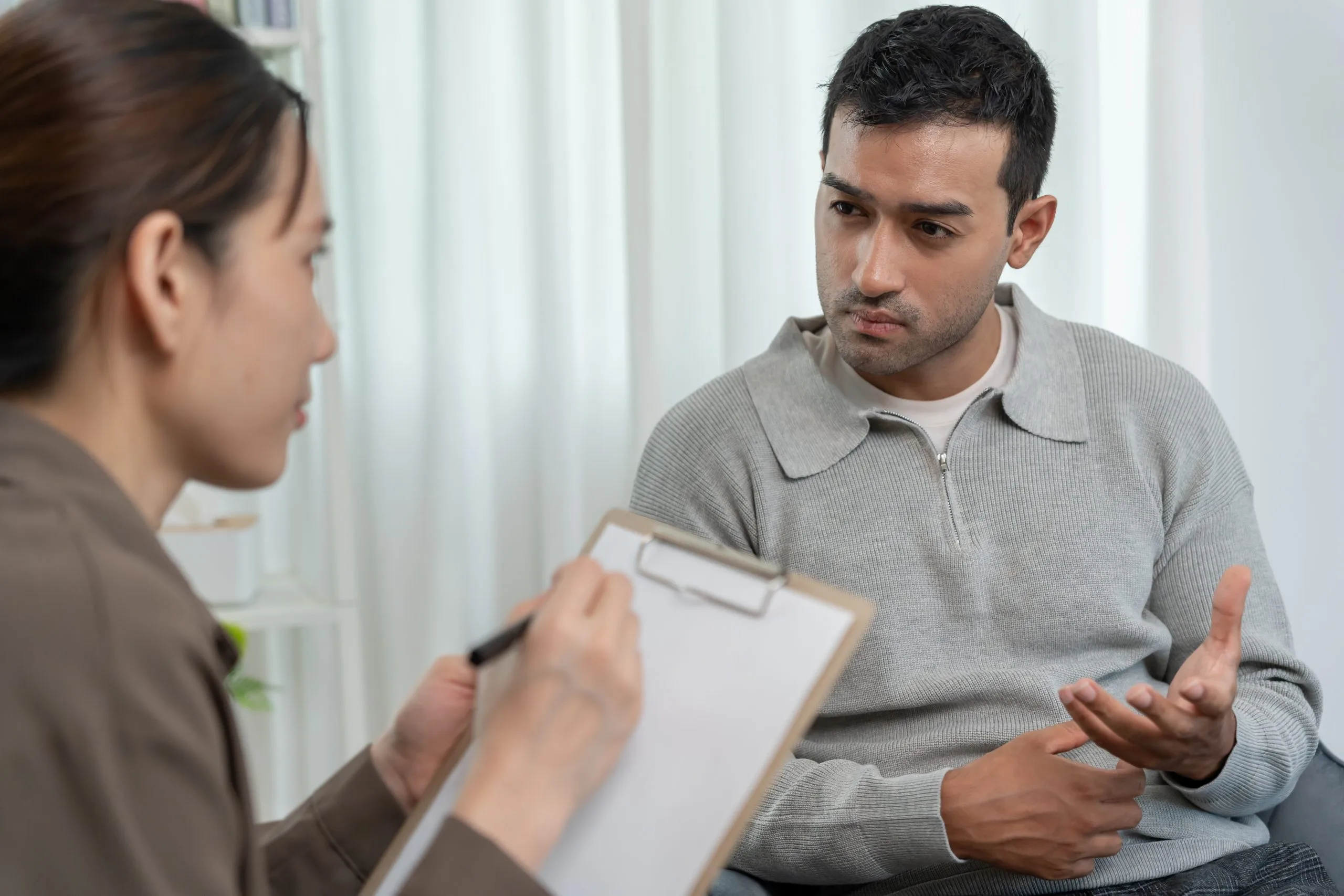 Man discussing mental health concerns with a psychiatrist taking notes during a consultation