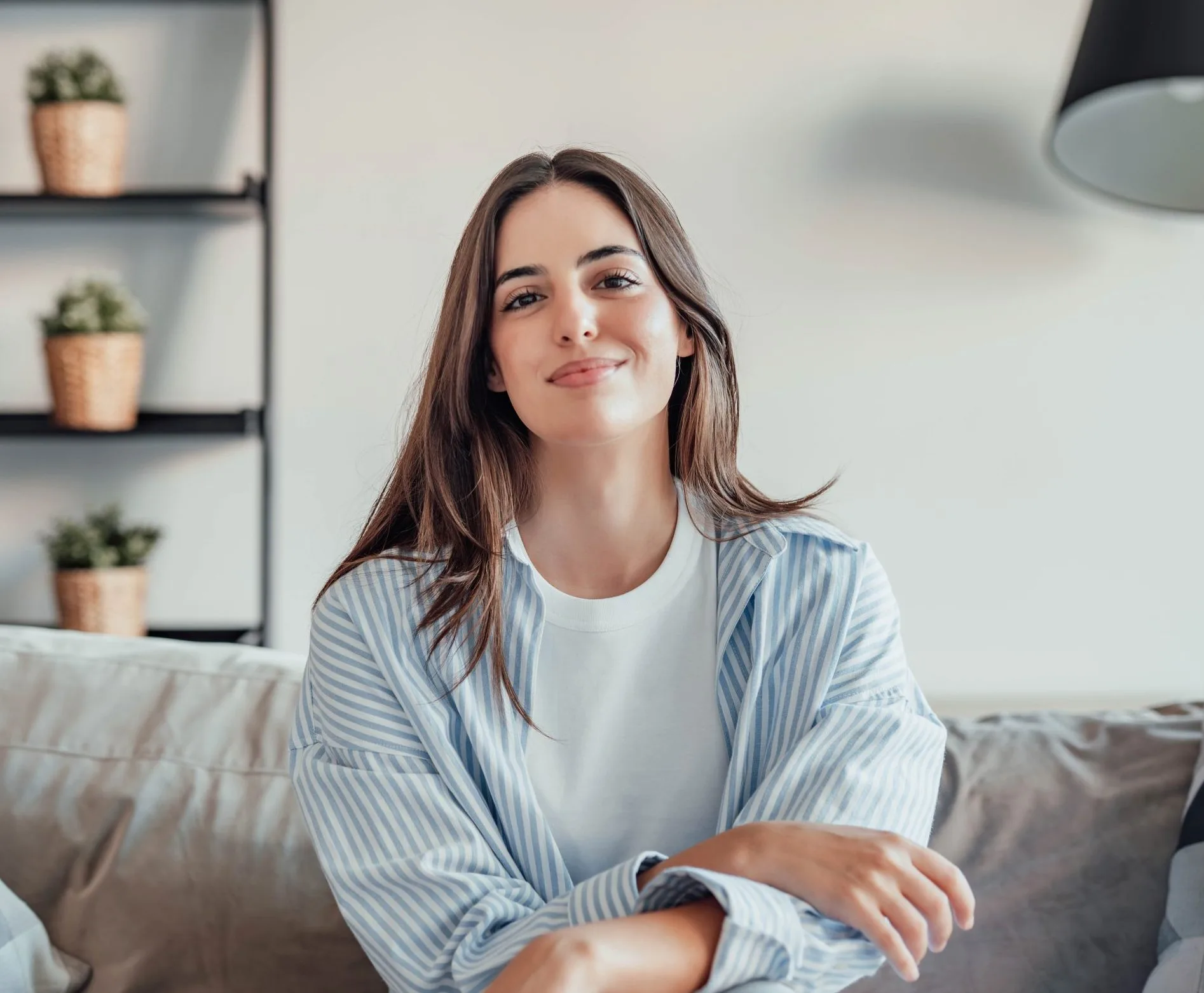 Woman sitting on a couch in a bright, modern office with potted plants on shelves behind her