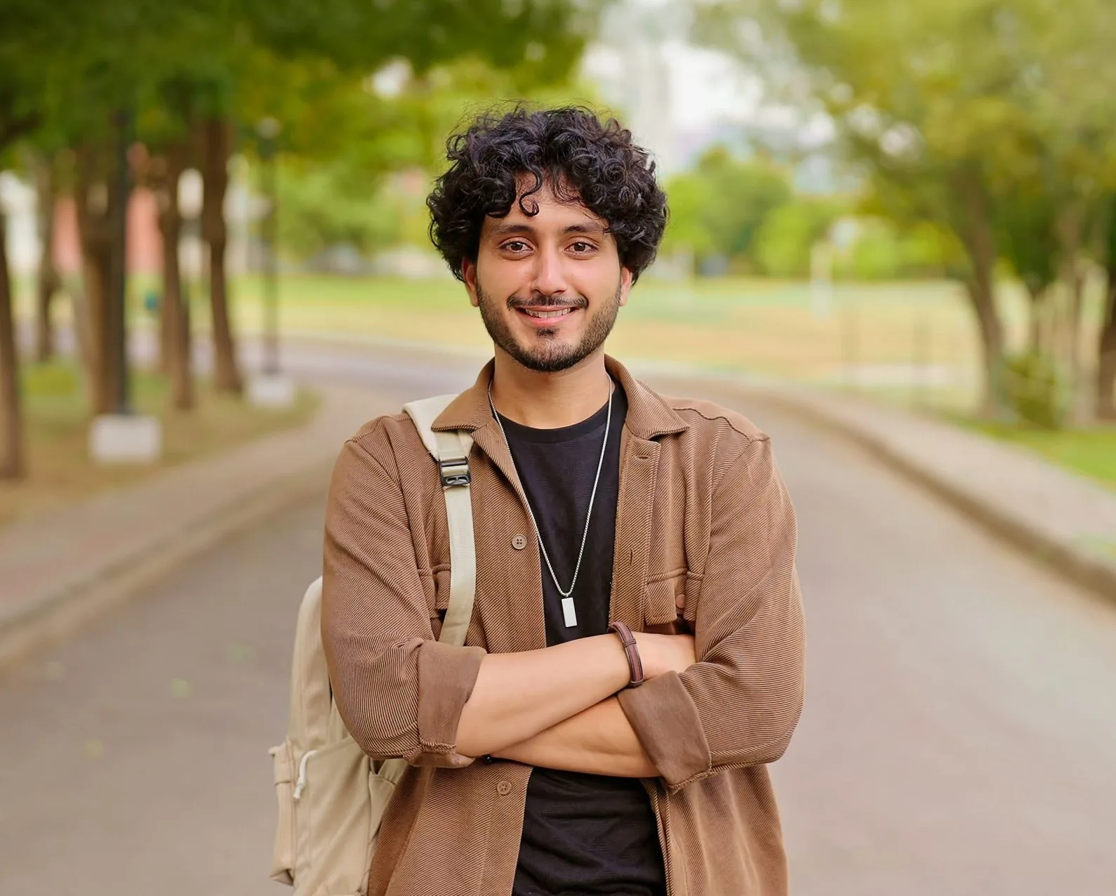 Smiling young man with backpack standing on a tree-lined campus path
