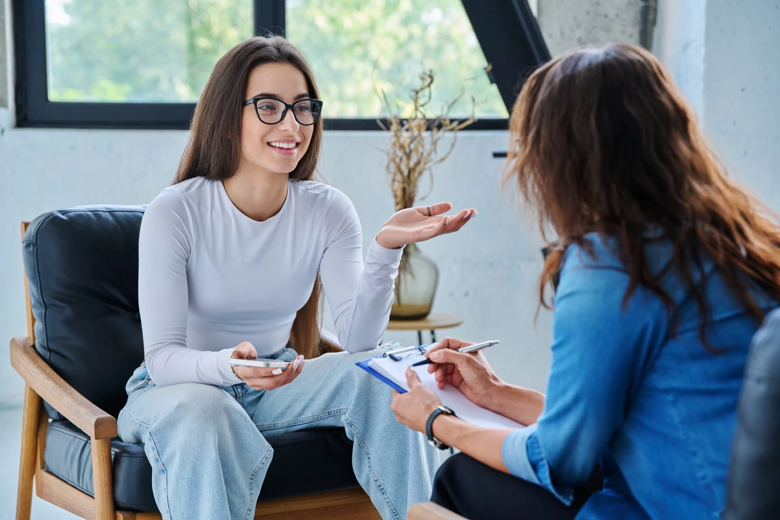 Therapist in glasses speaking with a patient during a counseling session in a modern office