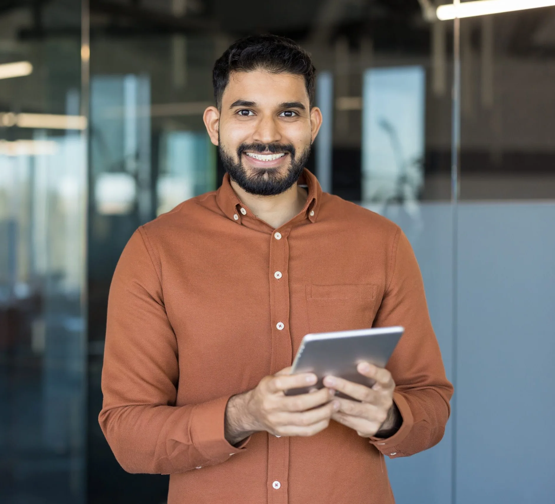 Man in rust-colored button-up shirt holding a tablet in a modern office setting