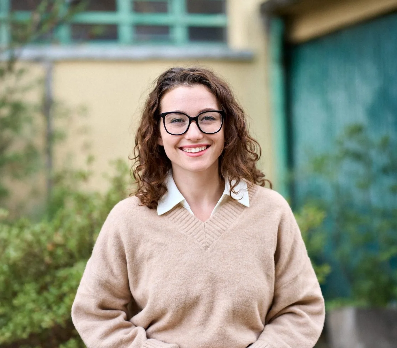 Woman wearing glasses and beige sweater smiling outdoors in front of a building