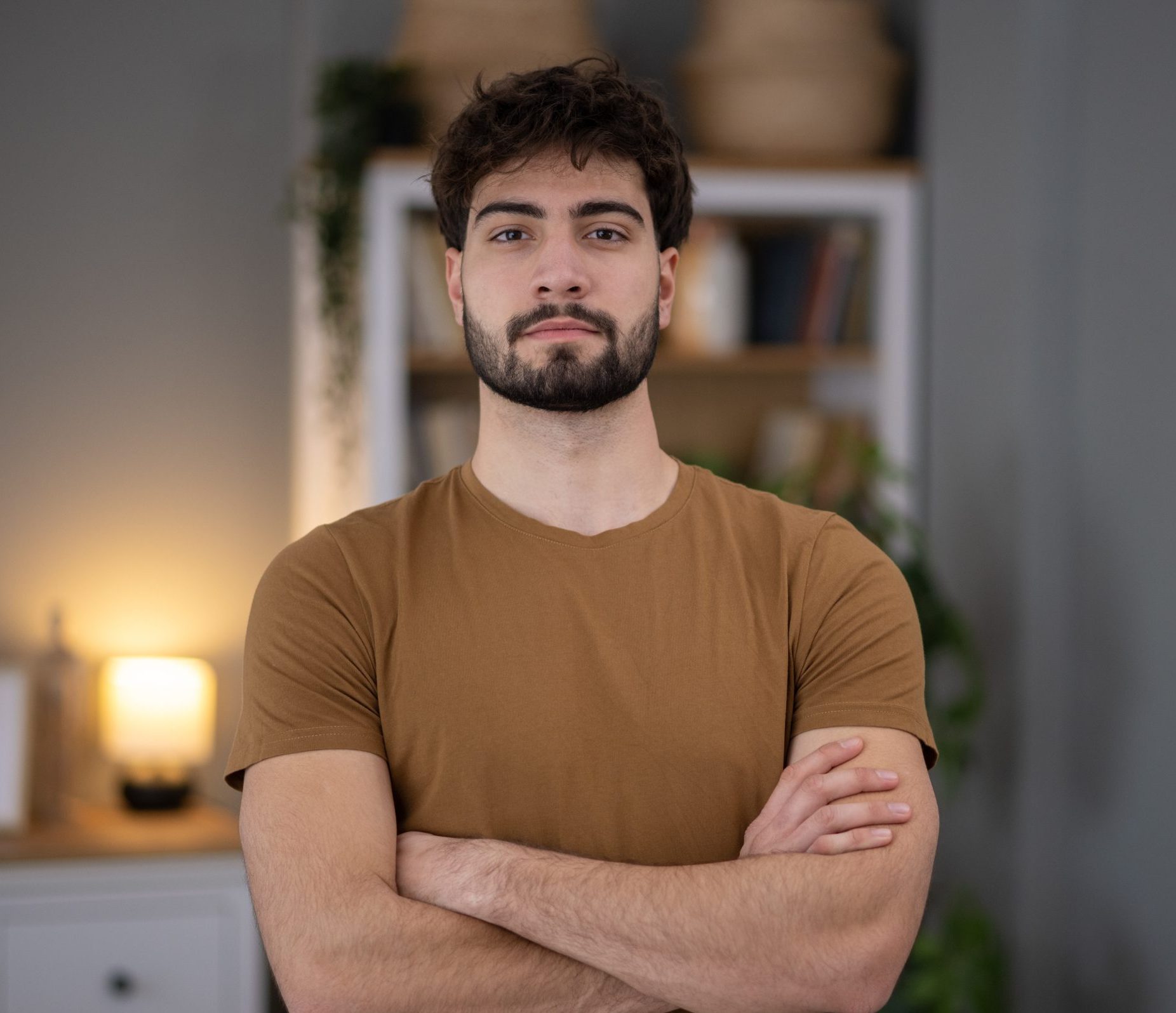 Man with arms crossed standing in a modern office setting with warm lighting