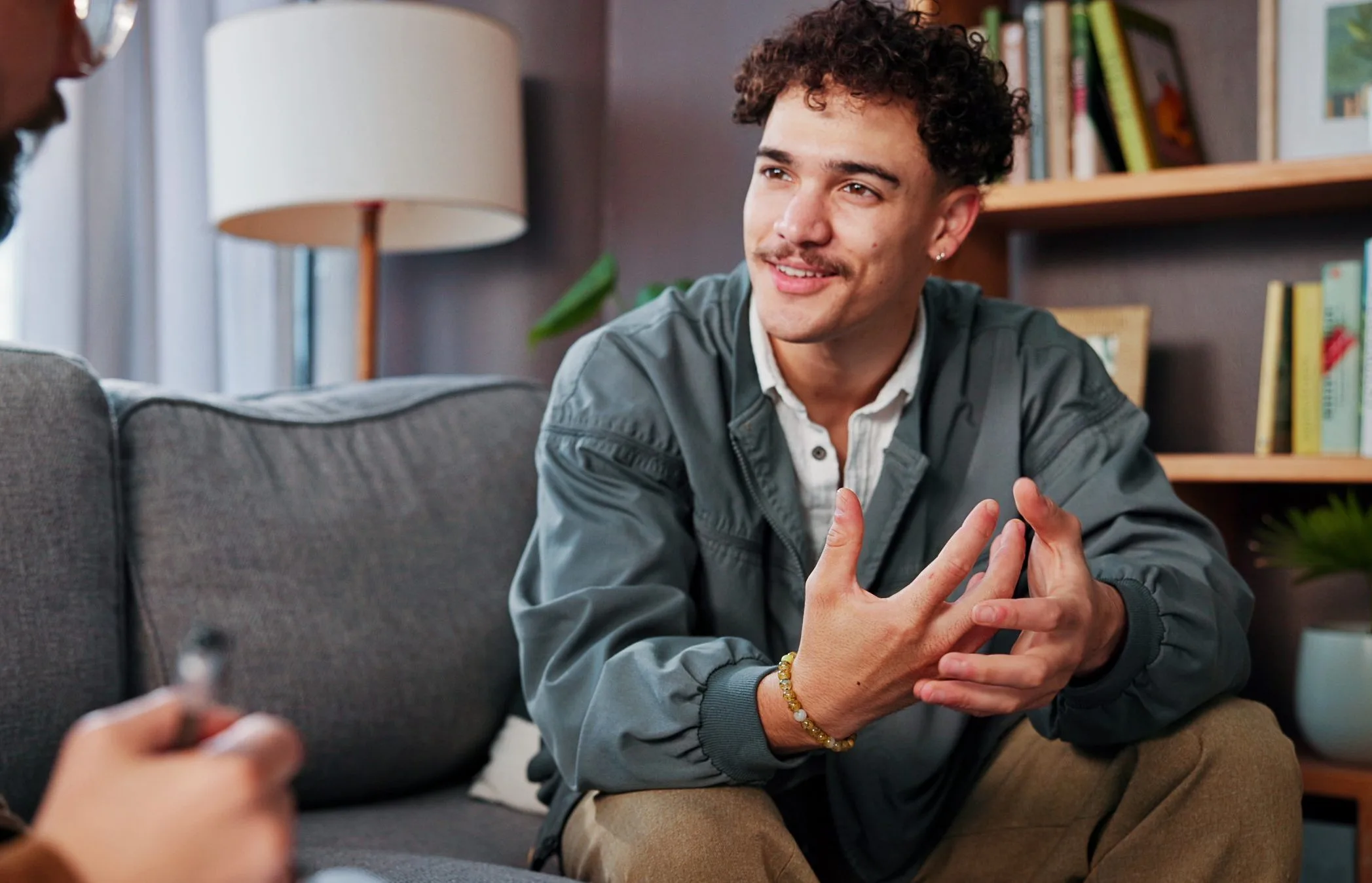 Man gesturing while speaking with a therapist in a comfortable office setting with bookshelves and a lamp