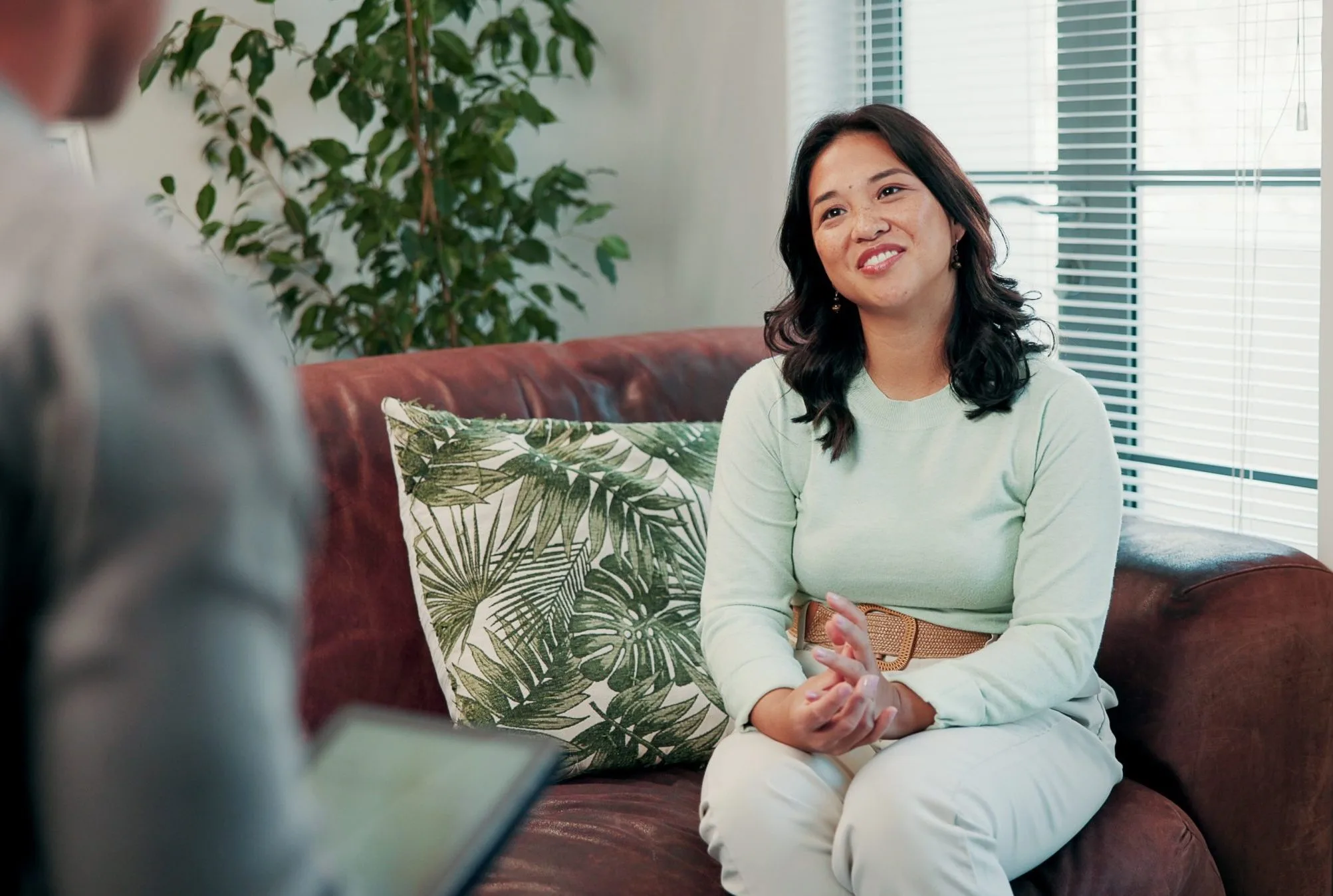 Woman in light green shirt sitting on burgundy couch during therapy session with clinician
