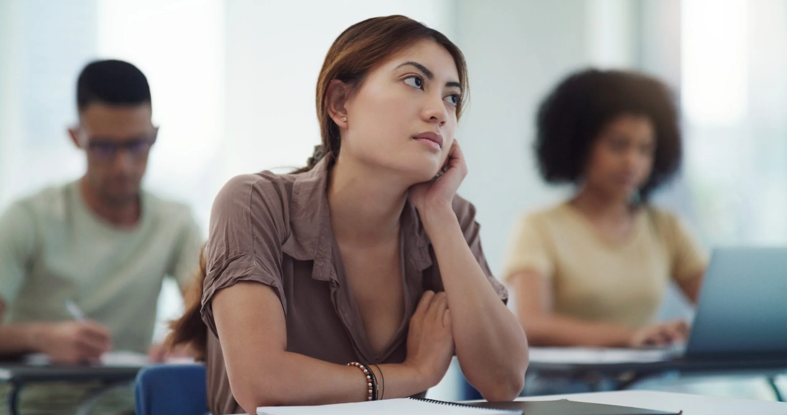 Woman in group therapy session looking thoughtful while others sit nearby with notebooks