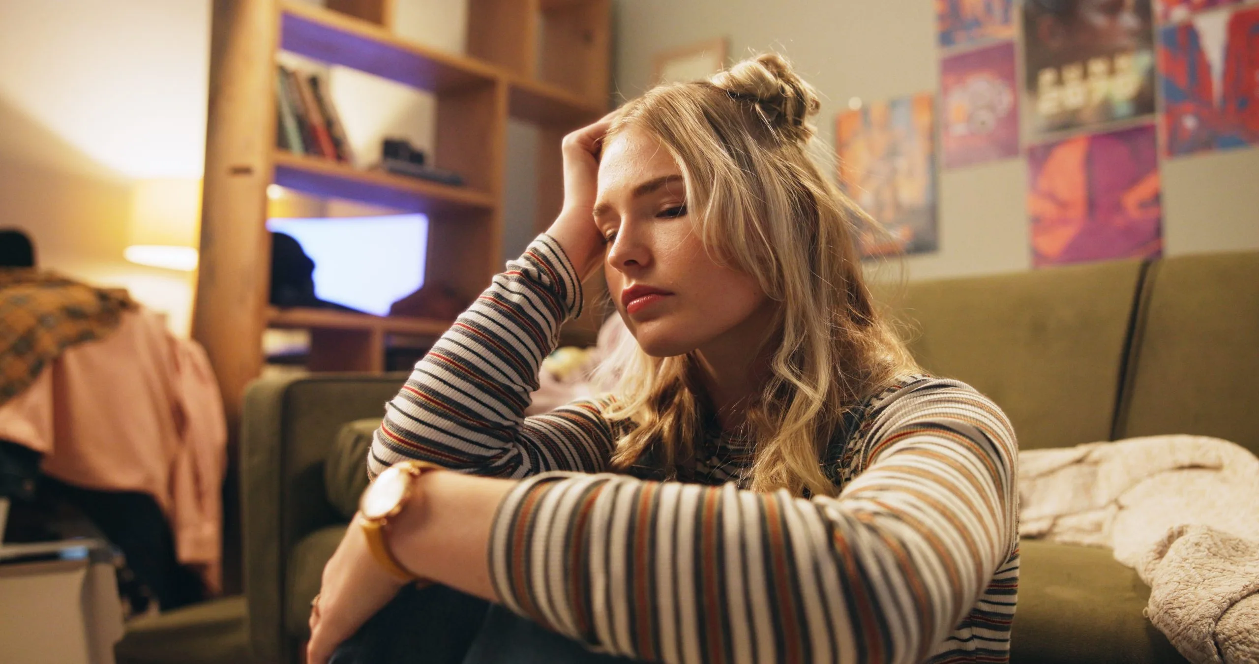 Woman in striped sweater sitting on couch with head resting on hand, appearing stressed or fatigued